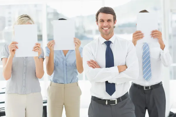 Empresario con colegas sosteniendo papel en blanco frente a la cara — Foto de Stock