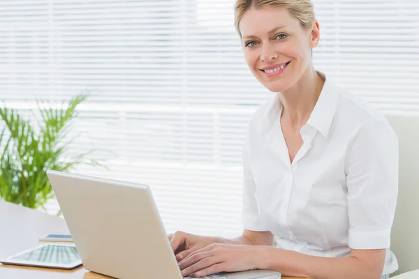 Mujer de negocios sonriente utilizando el ordenador portátil en el escritorio — Foto de Stock