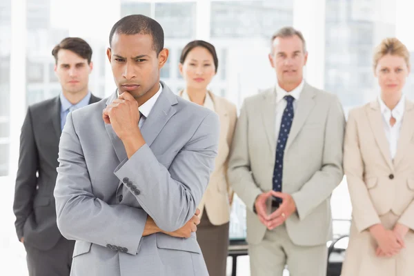 Serious businessman frowning at camera with team behind him — Stock Photo, Image