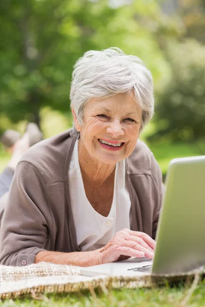 Smiling senior woman using laptop at park — Stock Photo, Image