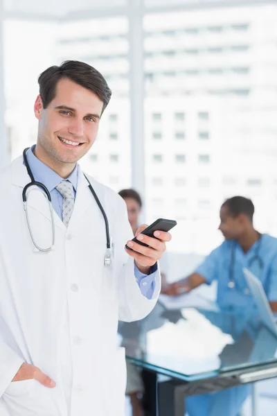 Doctor text messaging with group around table in hospital — Stock Photo, Image