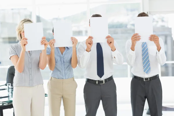 Business people with blank paper in front of faces in office — Stock Photo, Image
