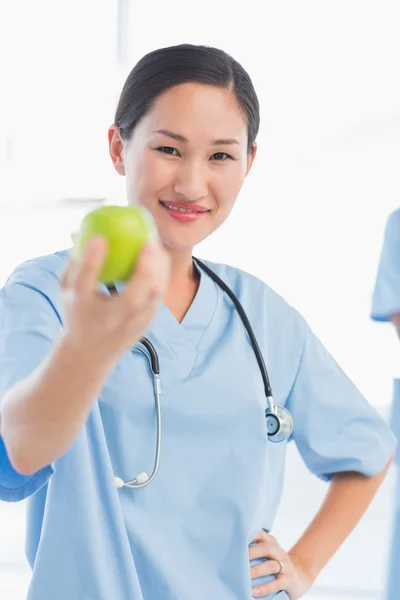 Smiling female surgeon holding out an apple in hospital — Stock Photo, Image