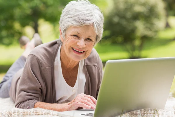 Usměvavá starší žena pomocí notebooku v parku — Stock fotografie