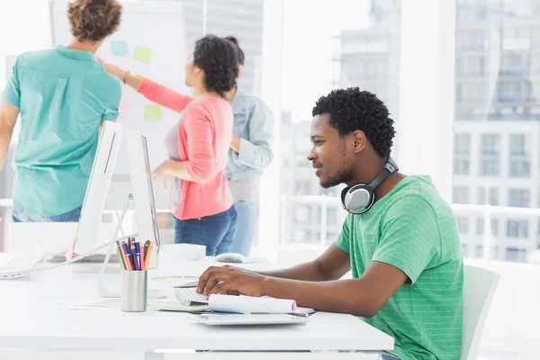 Homme occasionnel utilisant un ordinateur avec un groupe de collègues derrière en congé — Photo