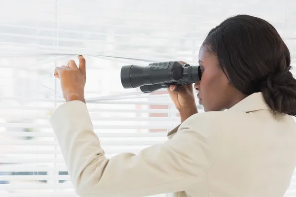 Businesswoman peeking with binoculars through blinds — Stock Photo, Image