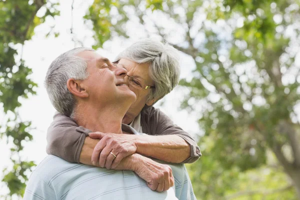 Senior woman embracing man from behind at park — Stock Photo, Image