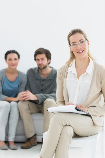 Female financial adviser with young couple in background — Stock Photo, Image