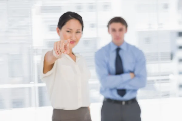 Businesswoman pointing towards camera with man in office — Stock Photo, Image