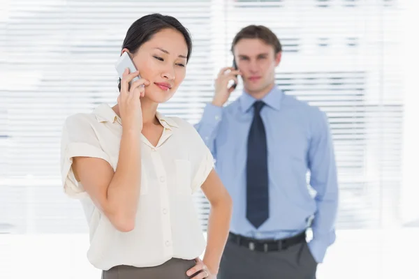 Empresaria y hombre usando teléfonos celulares en la oficina — Foto de Stock