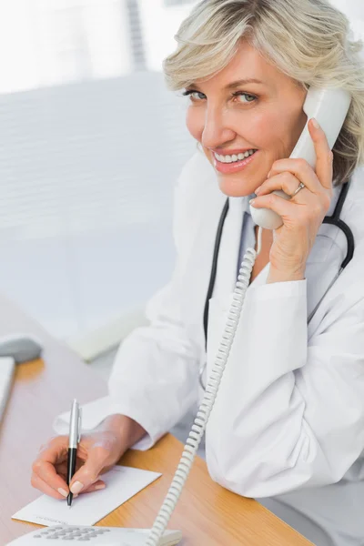 Médico femenino usando el teléfono mientras escribe notas — Foto de Stock