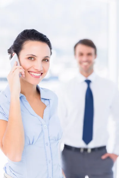 Woman on call with male colleague in background — Stock Photo, Image