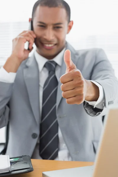 Smiling businessman gesturing thumbs up while on call — Stock Photo, Image
