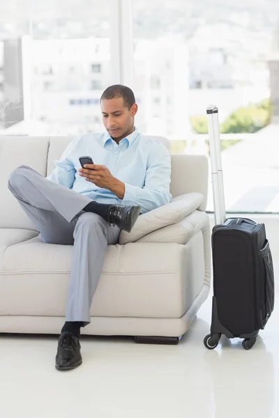 Empresario enviando un texto sentado en el sofá esperando para salir en viaje de negocios —  Fotos de Stock
