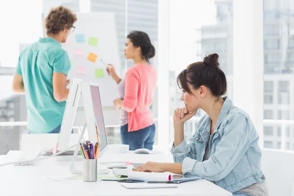 Femme occasionnelle utilisant un ordinateur avec des collègues derrière dans le bureau — Photo