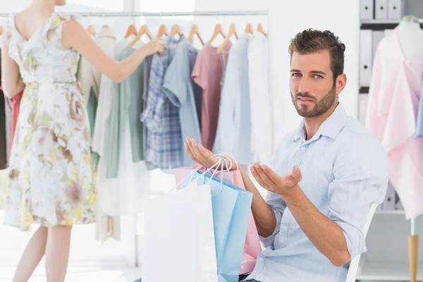 Gelangweilter Mann mit Einkaufstaschen, während Frau am Kleiderständer steht — Stockfoto