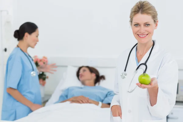 Улыбающийся доктор держит яблоко с пациентом в больнице — стоковое фото