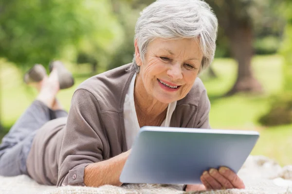 Lachende senior vrouw met behulp van digitale tablet in het park — Stockfoto
