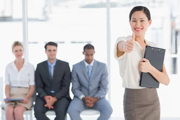 Woman gesturing thumbs up with people waiting for interview — Stock Photo, Image