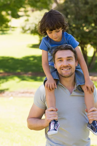 Sorrindo homem carregando filho em seus ombros no parque — Fotografia de Stock
