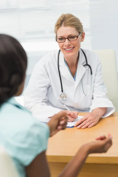 Médico sonriente escuchando a su paciente y tomando notas — Foto de Stock