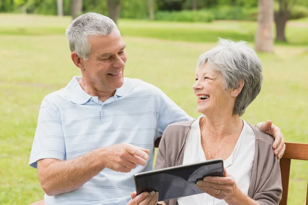 Casal sênior alegre usando tablet digital no banco no parque — Fotografia de Stock