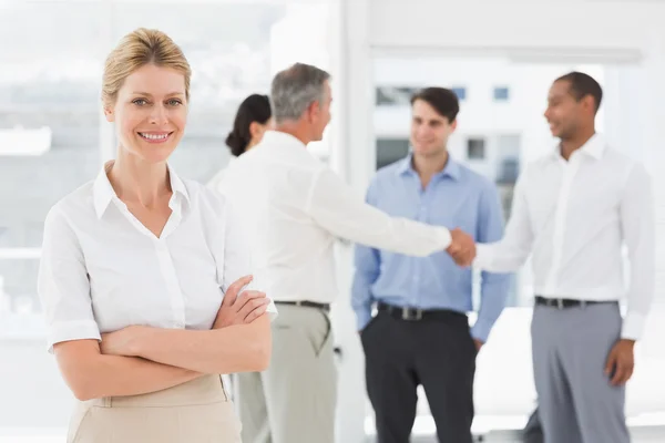 Rubia mujer de negocios con el equipo detrás de su sonrisa en la cámara — Foto de Stock