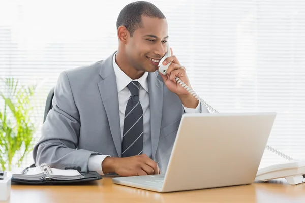 Businessman using laptop and phone at office desk — Stock Photo, Image
