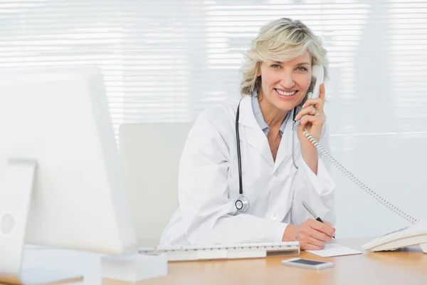 Médecin souriant avec ordinateur utilisant le téléphone au bureau médical — Photo