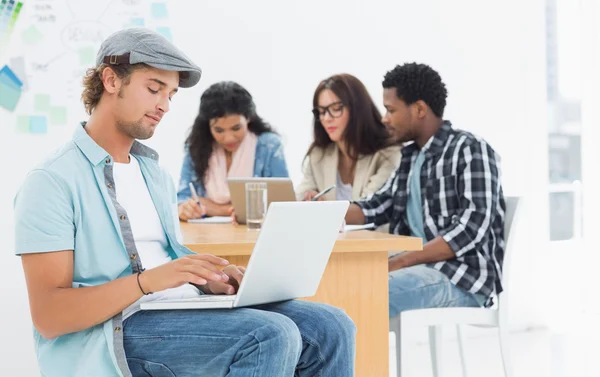 Homme décontracté utilisant un ordinateur portable avec des collègues derrière dans le bureau — Photo