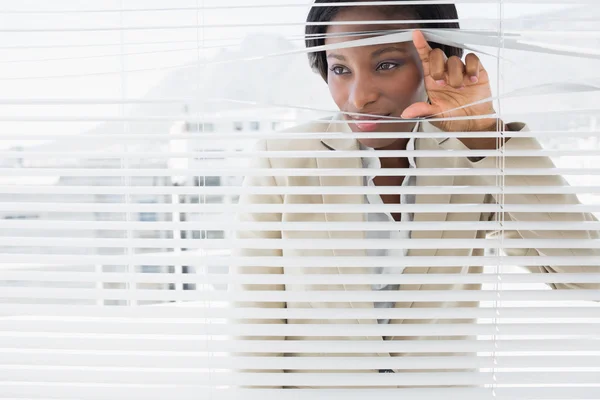 Businesswoman peeking through blinds — Stock Photo, Image