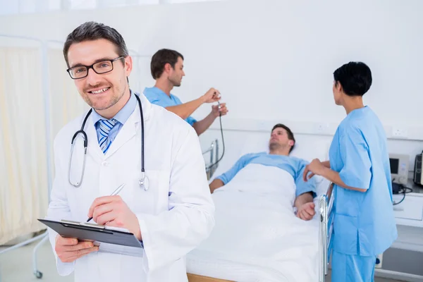 Doktor psaní zpráv s pacientem a chirurgů v pozadí — Stock fotografie