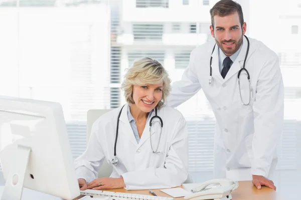 Médicos sonrientes con computadora en el consultorio médico — Foto de Stock