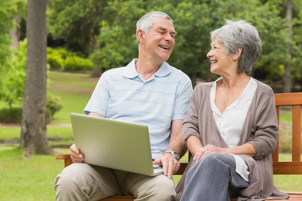 Coppia anziana allegra usando il computer portatile a parco — Foto Stock