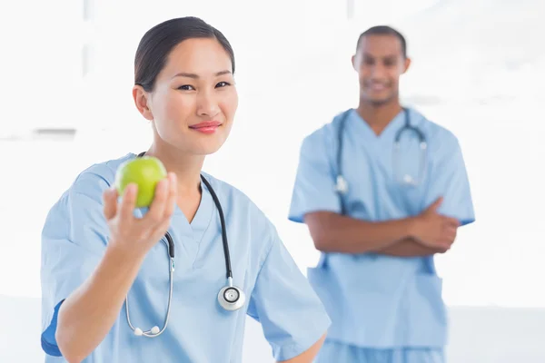 Cirujano sonriente sosteniendo una manzana con su colega en el hospital —  Fotos de Stock