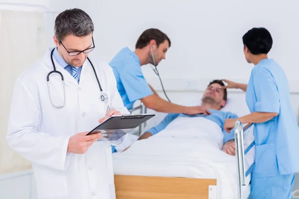 Doctor writing reports with patient and surgeons in background — Stock Photo, Image