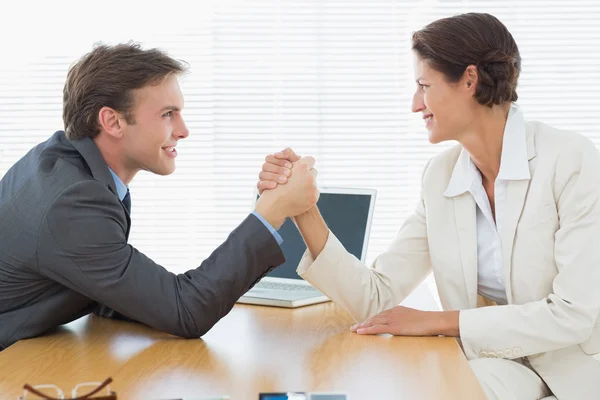 Smiling business couple arm wrestling at office desk — Stock Photo, Image