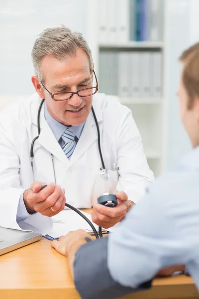 Médico sorrindo levando seus pacientes pressão arterial — Fotografia de Stock