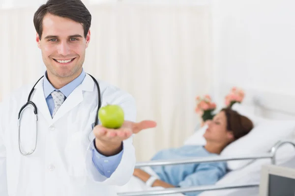 Smiling doctor holding apple with patient in hospital — Stock Photo, Image