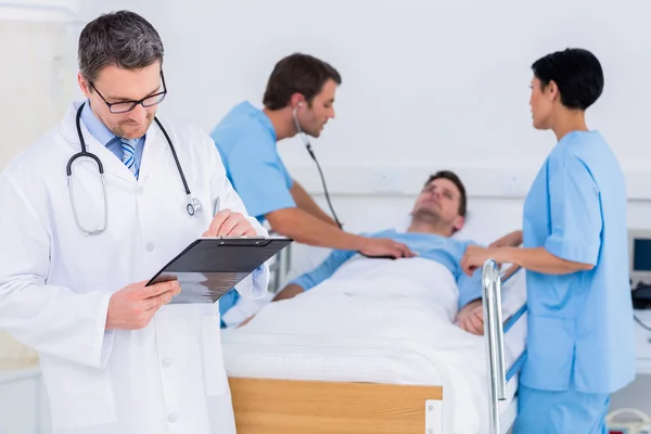 Doctor writing reports with patient and surgeons in background — Stock Photo, Image