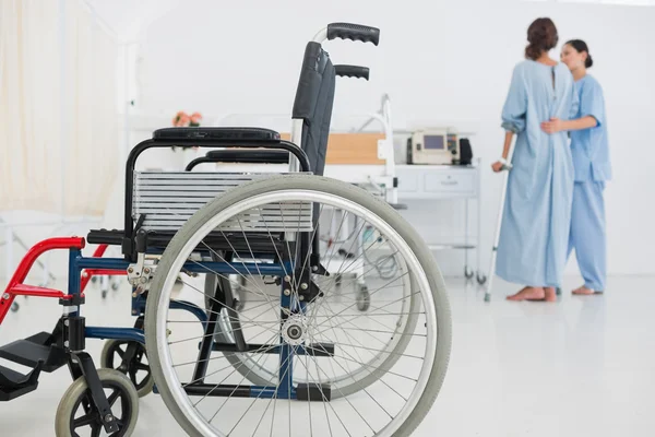 Arzt hilft Patient beim Gehen mit Rollstuhl im Vordergrund — Stockfoto