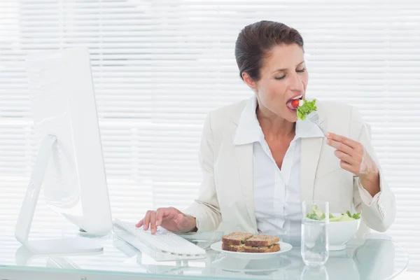 Femme d'affaires manger de la salade et en utilisant l'ordinateur au bureau — Photo