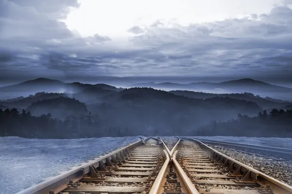 Trilhas de trem que levam a montanhas nebulosas — Fotografia de Stock