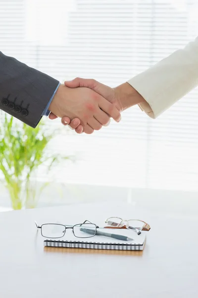 Close-up of shaking hands over eye glasses and diary — Stock Photo, Image