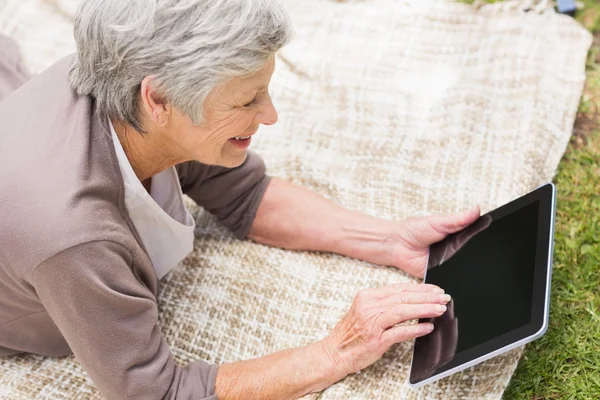 Lachende senior vrouw met behulp van digitale tablet in het park — Stockfoto