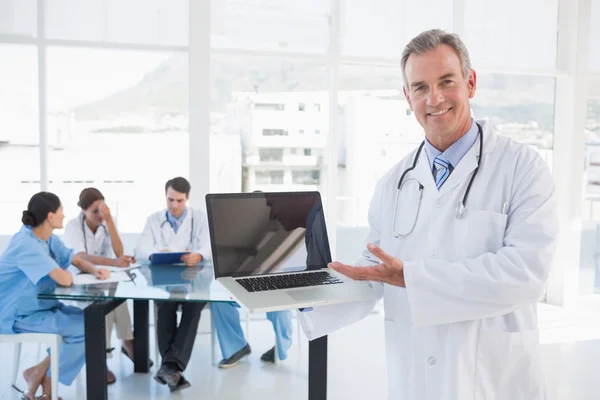 Läkaren håller laptop med gruppen runt bordet i sjukhus — Stockfoto