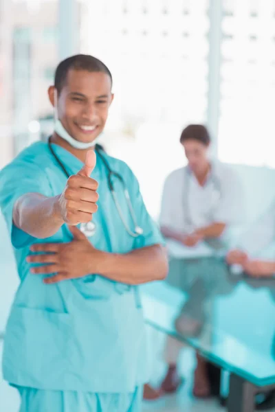 Surgeon gesturing thumbs up with group around table in hospital — Stock Photo, Image
