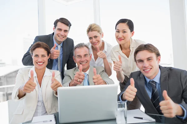 Business colleagues with laptop gesturing thumbs up at desk Stock Picture
