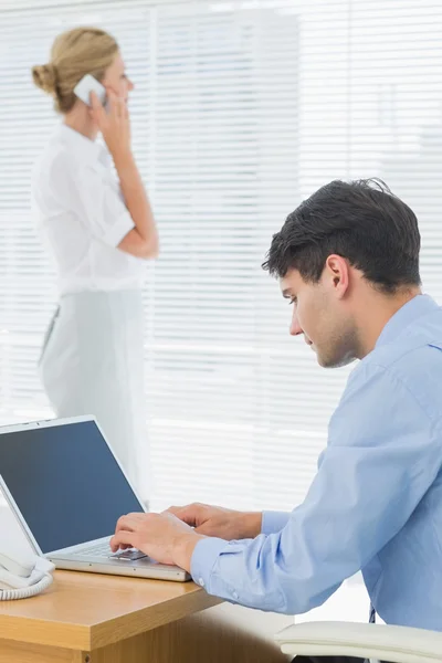 Uomo e donna d'affari che utilizzano cellulare e laptop in ufficio — Foto Stock