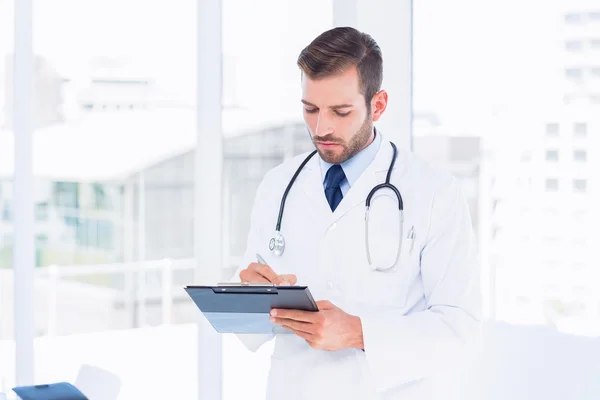 Médico masculino concentrado escribiendo informes en portapapeles — Foto de Stock